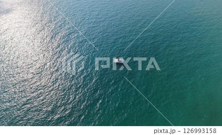 Catamaran sailing in calm turquoise water under sunlight reflection 126993158