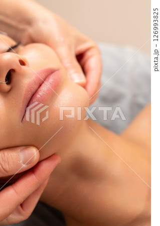 Close-up of a facial massage session, with hands gently massaging a woman s chin and jawline. 126993825