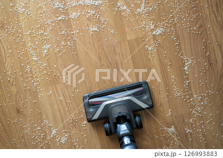 Vacuum cleaner nozzle picking up scattered rice grains from a wooden floor concept of cleaning, mess, and home maintenance. 126993883