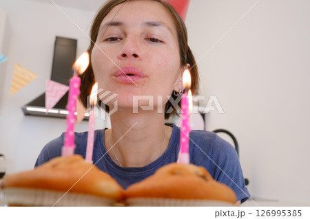 Woman celebrates with four cupcakes topped with candles in place of traditional birthday cake. Smiling and joyful, he enjoys cozy and unique celebration, creating warm and memorable festive moment. 126995385