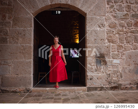 Woman in red dress walking narrow streets of old town Antalya during warm summer evening. Historic atmosphere and Mediterranean charm creates peaceful travel experience. near old mosque 126995430