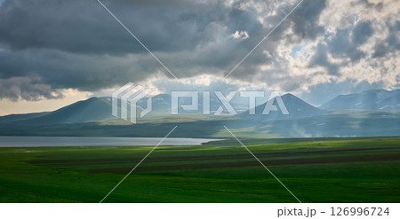 Sunlight breaks through clouds over serene mountains and a calm lake. High quality photo 126996724