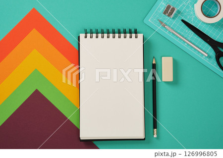 A blank sketchbook page with paper craft supplies in the background. Turquoise background, space for your text. 126996805