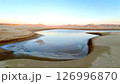 Salty lake curves through layered erosion along bright desert walls, blue water contrasts warm sunset reflections, showing eco value of rare water formation in arid terrain. 126996870