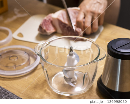 Woman cuts the meat, prepares it to grind it in electrical chopper Woman cuts the meat, prepares it to grind it in electrical chopper 126998080