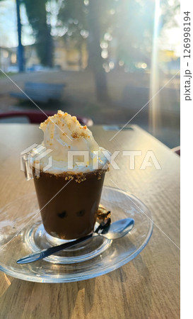 Espresso in a small transparent glass with a mound of cream on top and a sprinkle of cookies against the background of a park. The concept of rest, coffee break, relaxation, coffee business. 126998194