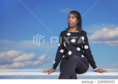 African Woman Sitting Outdoors Against Blue Sky is the limit with Clouds African Woman Sitting Outdoors Against Blue Sky is the limit with Clouds 126998381