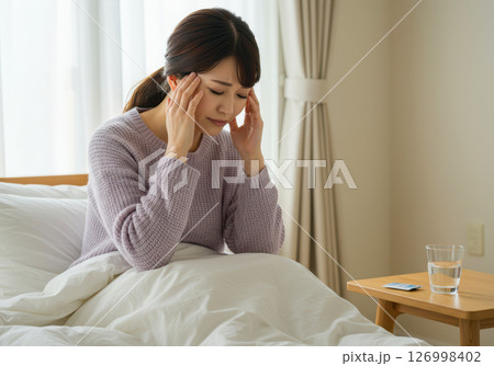 頭痛でこめかみを押さえベッドで休む女性(AI生成画像) 頭痛でこめかみを押さえベッドで休む女性(AI生成画像) 126998402