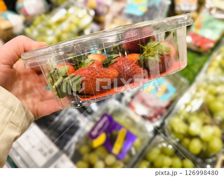 strawberries in containers in person's hand on blurred background of supermarket shelves close-up. plastic strawberry container in a woman's hand 126998480