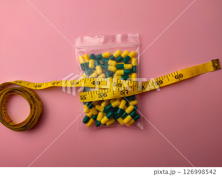 Top view of a medicine pill package with measuring tape on a pink background. 126998542