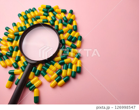 Medicine pill and magnifying glass on a pink background with copy space. Medicine pill and magnifying glass on a pink background with copy space. 126998547