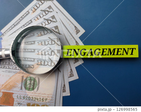 Banknotes and magnifying glass with the word ENGAGEMENT on a blue background. 126998565