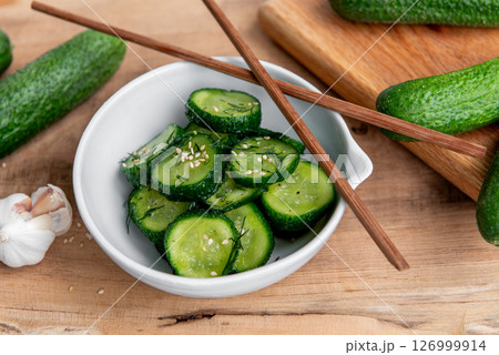Cucumber salad. Cucumbers slices in a ceramic white bowl on a wooden table. Cucumber salad. Cucumbers slices in a ceramic white bowl on a wooden table. 126999914