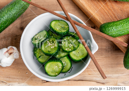 Cucumber salad. Cucumbers slices in a ceramic white bowl on a wooden table. Cucumber salad. Cucumbers slices in a ceramic white bowl on a wooden table. 126999915