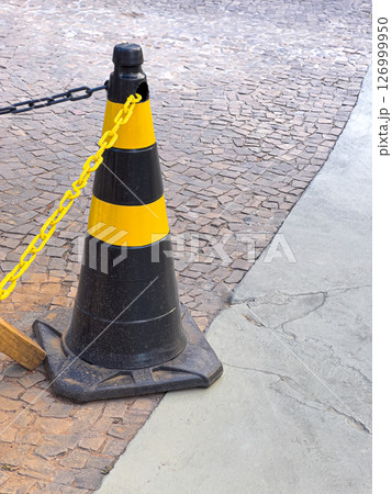 Black and yellow traffic cone on urban cobblestone pavement and concrete sidewalk corner 126999950