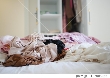 Messy pile of folded clothes on bed in a bright room 127003056