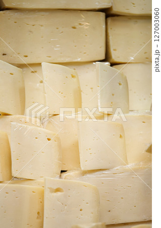 Freshly cut cheese blocks neatly stacked in a market stall 127003060
