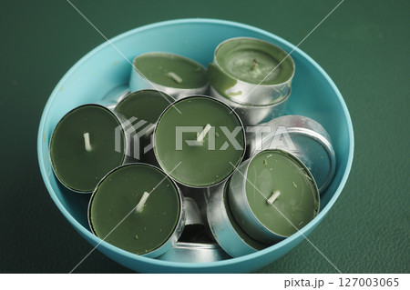 Candles in green holders arranged in a blue bowl on a surface Candles in green holders arranged in a blue bowl on a surface 127003065