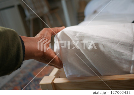 Hand adjusting white bedding on a wooden bed frame 127003432