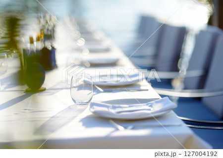 A row of empty plates on a long table with a white tablecloth. A table in a Mediterranean restaurant ready to serve a large group of visitors or tourists. A row of empty plates on a long table with a white tablecloth. A table in a Mediterranean restaurant ready to serve a large group of visitors or tourists. 127004192