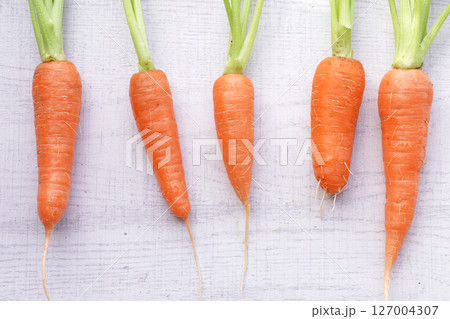 Organic mini carrots with leaves isolated on white wood background. Organic mini carrots with leaves isolated on white wood background. 127004307