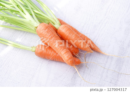 Organic mini carrots with leaves isolated on white wood background. Organic mini carrots with leaves isolated on white wood background. 127004317