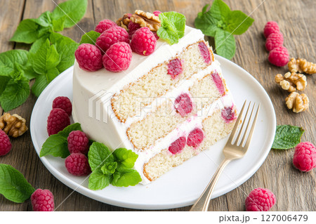 Delicious Cake Slice with Raspberries and Walnuts on a White Plate Surrounded by Fresh Mint 127006479