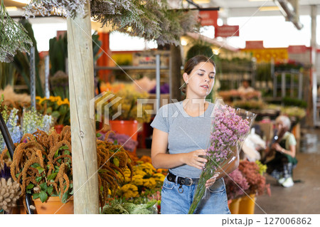 Young woman customer choosing bundle of limonium in open-air plants market 127006862