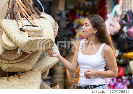 Girl choosing fashionable straw bag with interest at street market 127006885