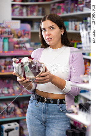 Attractive girl choosing gift set of bottles shampoo and hair balms in cosmetics store Attractive girl choosing gift set of bottles shampoo and hair balms in cosmetics store 127006912