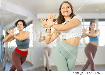 Cheerful young female instructor leading Zumba class for women Cheerful young female instructor leading Zumba class for women 127006928