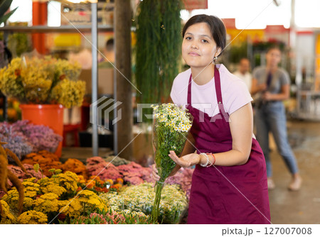 Asian female florist offering bouquet of blooming daisies at flower market 127007008
