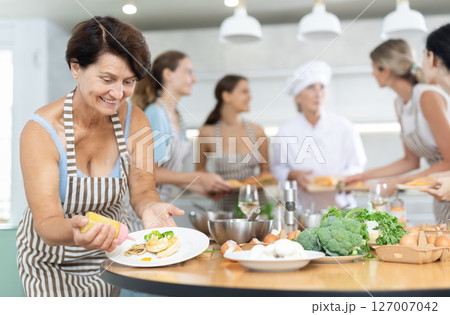 Mature woman decorating cooked chicken breast with mustard Mature woman decorating cooked chicken breast with mustard 127007042