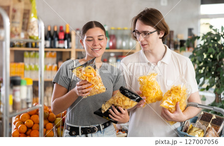 European youth girl and guy choose and buy chips and potato mix crisps in store 127007056