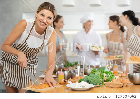 Girl at group class of culinary school cuts up chicken and prepares low-calorie diet lunch 127007062