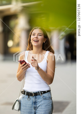 Young smiling girl with phone walks along city street 127007136