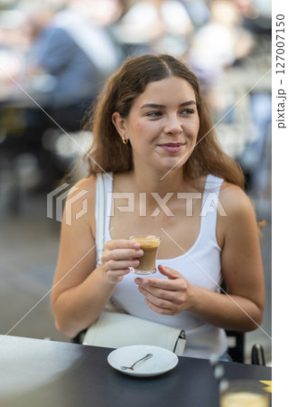 Girl relaxes in street cafe, drinks coffee Girl relaxes in street cafe, drinks coffee 127007150