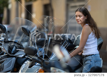 Young woman parking scooter in city street on summer day 127007178