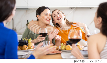 Girlfriends chatting and drinking wine in kitchen 127007356