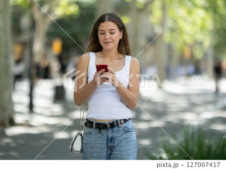 Girl looks at smartphone screen while walking Girl looks at smartphone screen while walking 127007417