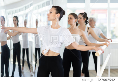 Girls in ballet class perform second position with participation of mature female mentor 127007542