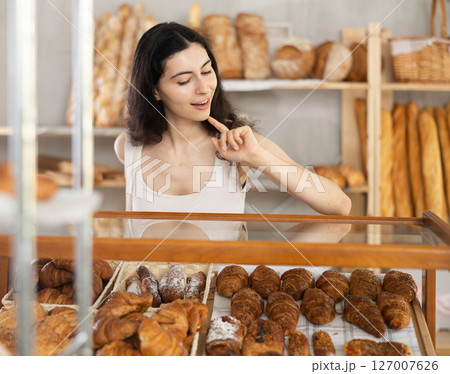 Young woman near window of bakery food court store examines assortment Young woman near window of bakery food court store examines assortment 127007626