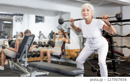 Mature sportswoman doing exercises with a barbell and dumbbells in gym 127007656