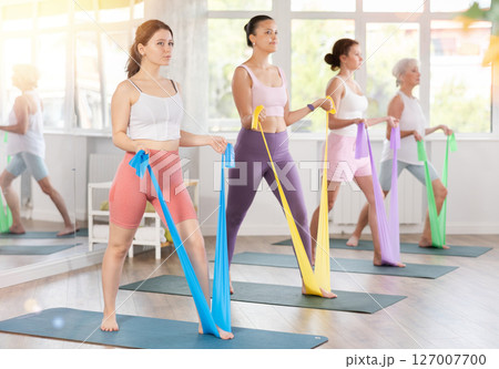 Women are doing stretching exercise with resistance bands in gym. Teamwork, good mood and healthy lifestyle concept Women are doing stretching exercise with resistance bands in gym. Teamwork, good mood and healthy lifestyle concept 127007700