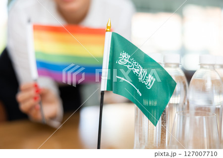 Little flag of Saudi Arabia on table and LGBT flag put next to it by young woman Little flag of Saudi Arabia on table and LGBT flag put next to it by young woman 127007710