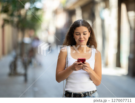 Young girl with mobile phone in her hands walking around the city and taking pictures of sights Young girl with mobile phone in her hands walking around the city and taking pictures of sights 127007711