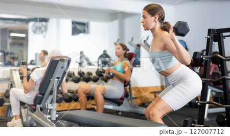 Focused sporty girl performing set of exercises with barbell during intense workout. Concept of weight training Focused sporty girl performing set of exercises with barbell during intense workout. Concept of weight training 127007712