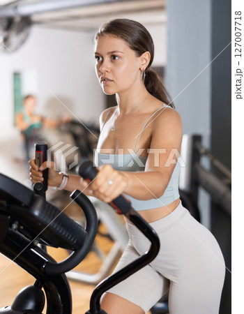 Portrait of sporty woman doing cardio workout on elliptical cross trainer at fitness center 127007718