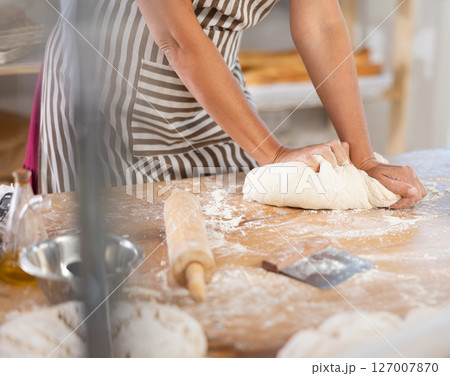 Closeup on pastry chef female hands kneading dough on table at bakery, culinary arts 127007870