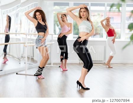 During lesson, girl learn to move and perform dance in heels with women companions During lesson, girl learn to move and perform dance in heels with women companions 127007894